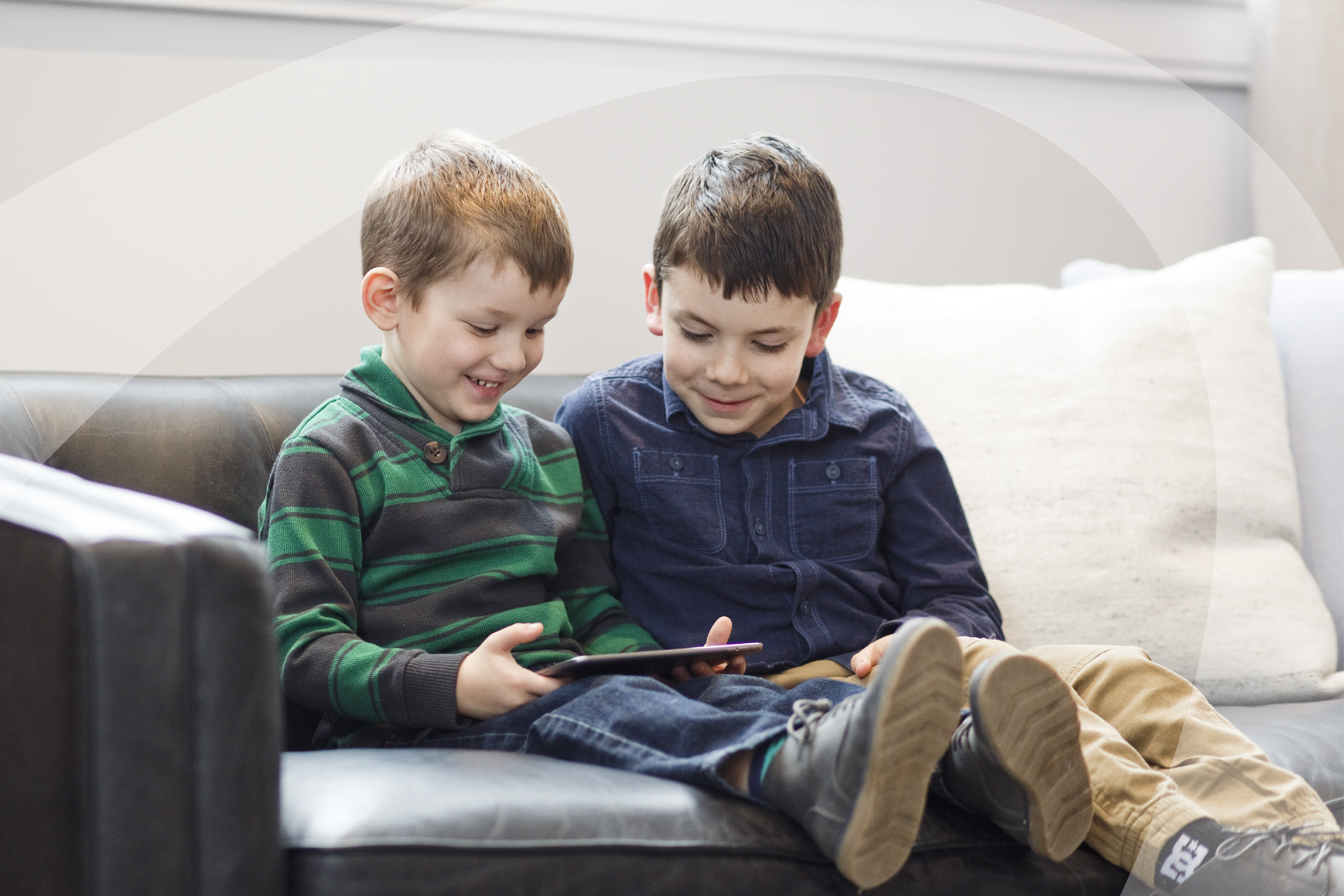 Two boys, smiling and playing on an iPad. 